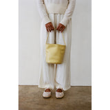 Person holding a yellow bag wearing a white outfit against a plain background.
