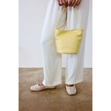 Person holding a yellow handbag wearing white pants and light-colored shoes on a plain background.