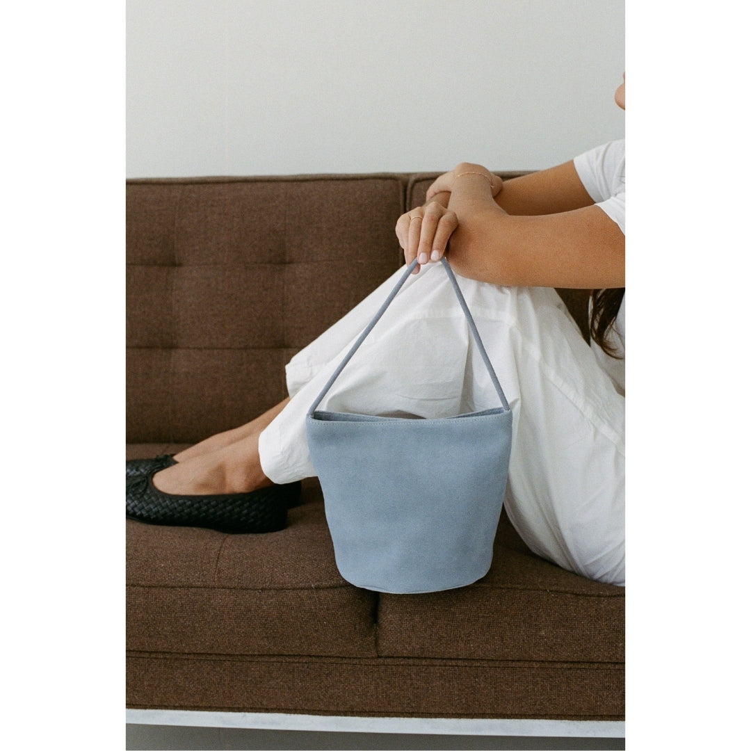 A person holding a blue suede handbag sitting on a brown couch.