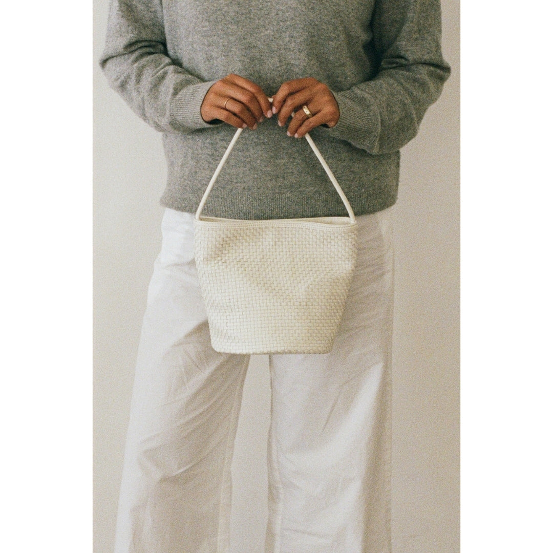 Person holding a white woven handbag against a plain background.