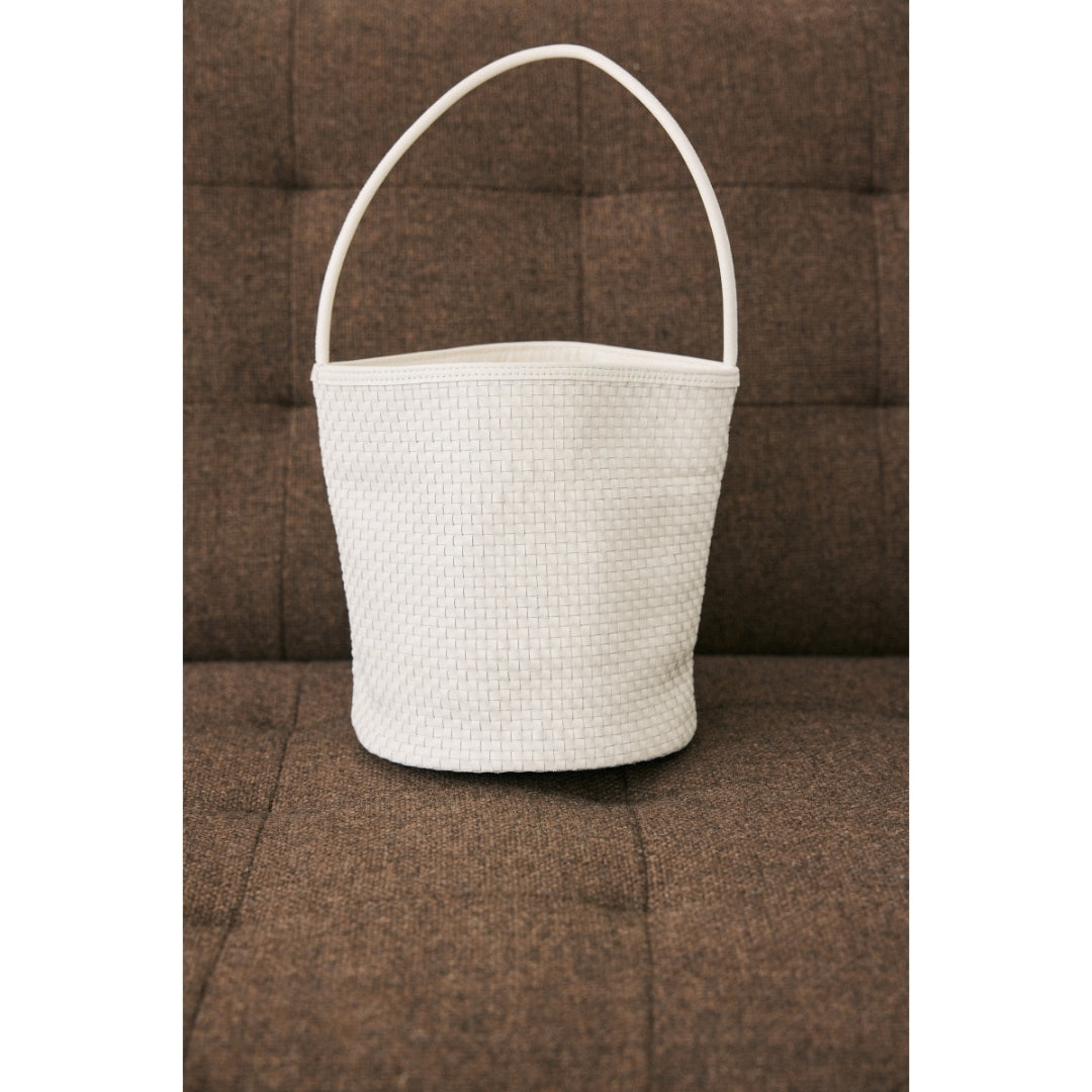 An ivory woven handbag on a brown couch.