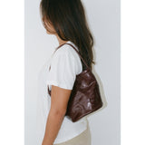A person wearing a white shirt with a burgundy handbag on their should against a white background.