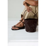 Person wearing black sandals and holding a burgundy leather bucket on a white background.