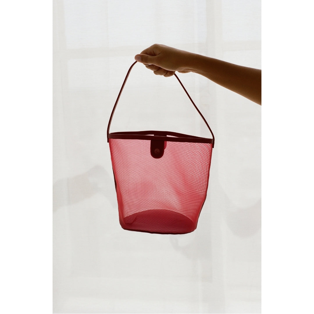 Hand holding a red mesh handbag against a white background.