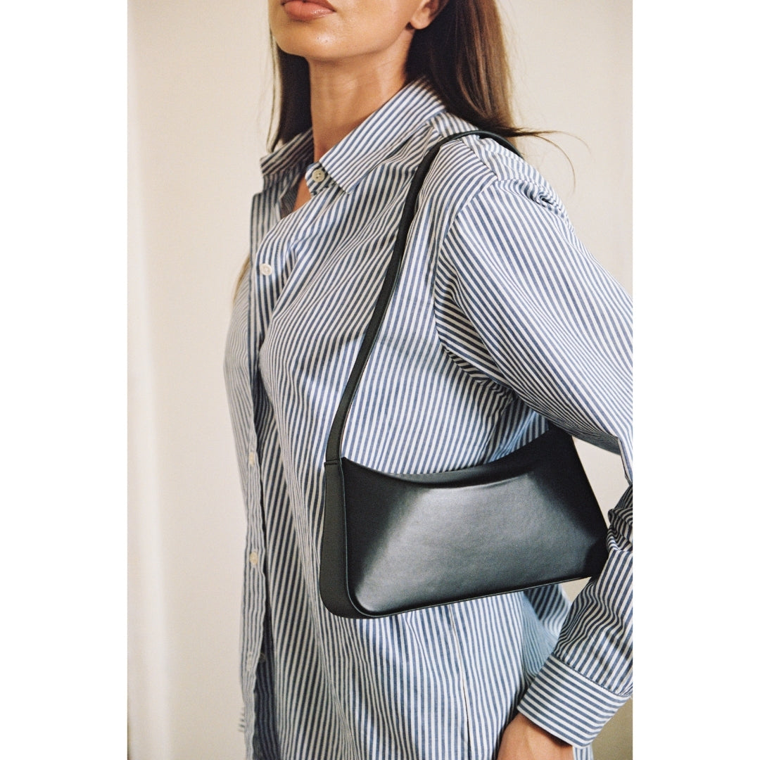 Woman wearing a black shoulder bag with a neutral background.