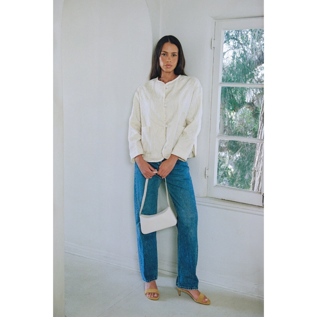 Woman wearing a white blouse and blue jeans standing in a room with a window.