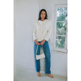 Woman wearing a white blouse and blue jeans standing in a room with a window.