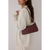 Person wearing a white sweater with a burgundy shoulder bag on a plain background.