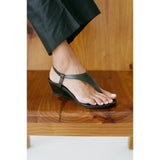 Black wedge sandal worn on a foot with a wooden floor background.