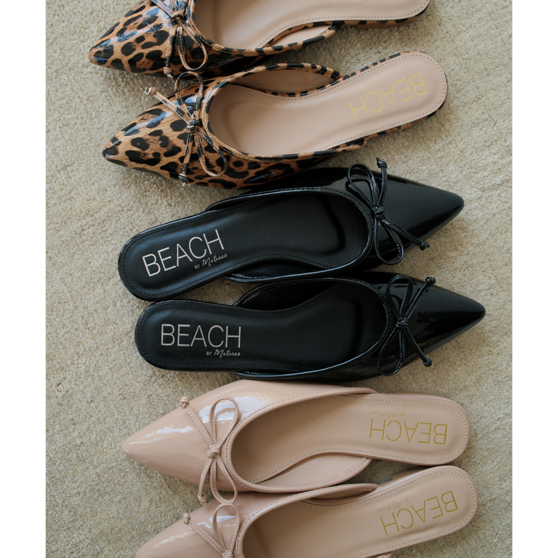 Reggie Vegan Pointed Toe Mule – Beach by Matisse – Black faux patent leather flat mule with pointed toe and petite bow detail.
