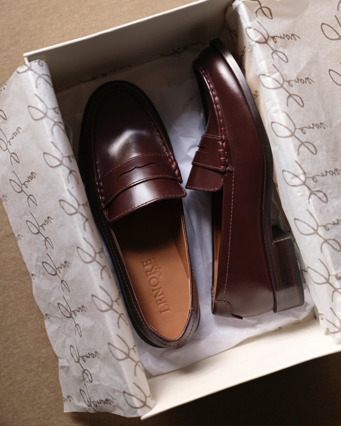 Pair of burgundy loafers in a box with branded tissue paper