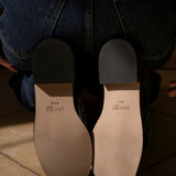 Close-up of a person wearing blue jeans with the sole of the shoes showing the brand 'Lenore'.